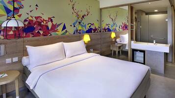 A hotel room with a bed, bedside lamps, a small table, a mirror, and a bathroom with a sink.