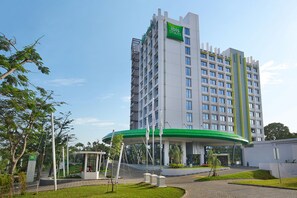 A modern hotel with a green and white facade, multiple floors, and a covered entrance area.