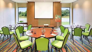 A conference room with a round table, green chairs, a projector screen, and a carpeted floor.