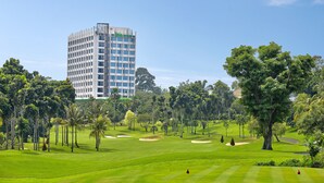 Un hotel moderno con un edificio alto, rodeado por un campo de golf bien cuidado con bunkers de arena y abundante vegetación.
