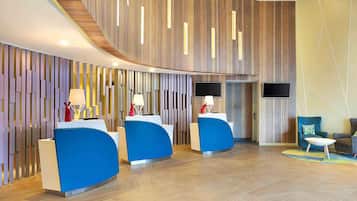 A modern reception area with curved wooden panels, two blue reception desks, and a flat-screen TV mounted on the wall.