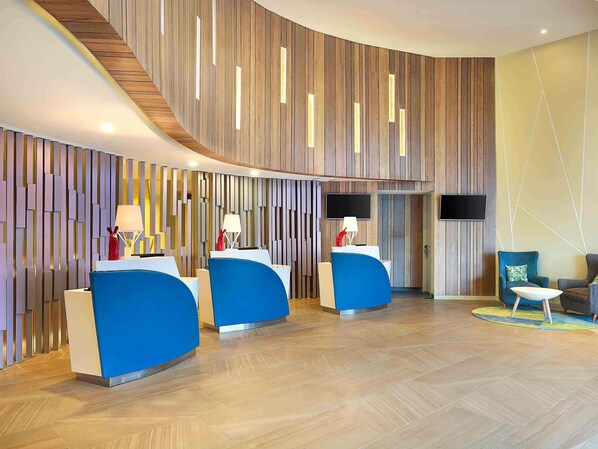 Una zona de recepción moderna con paneles de madera curvados, dos mostradores de recepción azules y un televisor de pantalla plana montado en la pared.