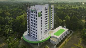 Un hotel moderno con una torre central, un cuerpo anexo de techo plano y un paisaje verde circundante.