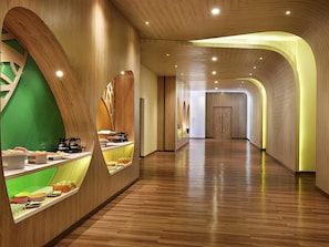 A modern hotel corridor with wooden paneling, a food display, and a long, open space leading to a door. - ibis Styles Bogor Raya (Bogor)