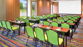 A conference room with green chairs, wooden tables, and a projector screen.