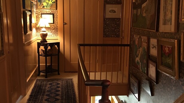 A staircase with a wooden handrail, a patterned rug, and framed artwork on the walls. - The Chestnut House (Nantucket)