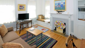 A living room with a sofa, television, fireplace, and a painting on the wall. - The Chestnut House (Nantucket)