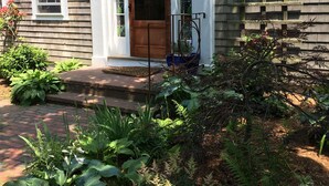 A house with a front porch, a wooden door, and a brick pathway leading to the entrance. - The Chestnut House (Nantucket)