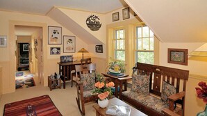 A cozy living room with a sofa, chairs, a coffee table, and a rug. There are framed pictures on the walls and a staircase leading to another level. - The Chestnut House (Nantucket)