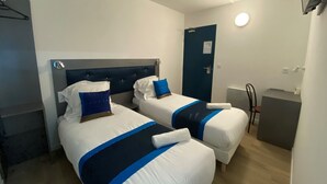 Une chambre d’hôtel avec deux lits, chacun recouvert d’une couvre-lit bleue et blanche, doté d’une tête de lit et d’une table de chevet.