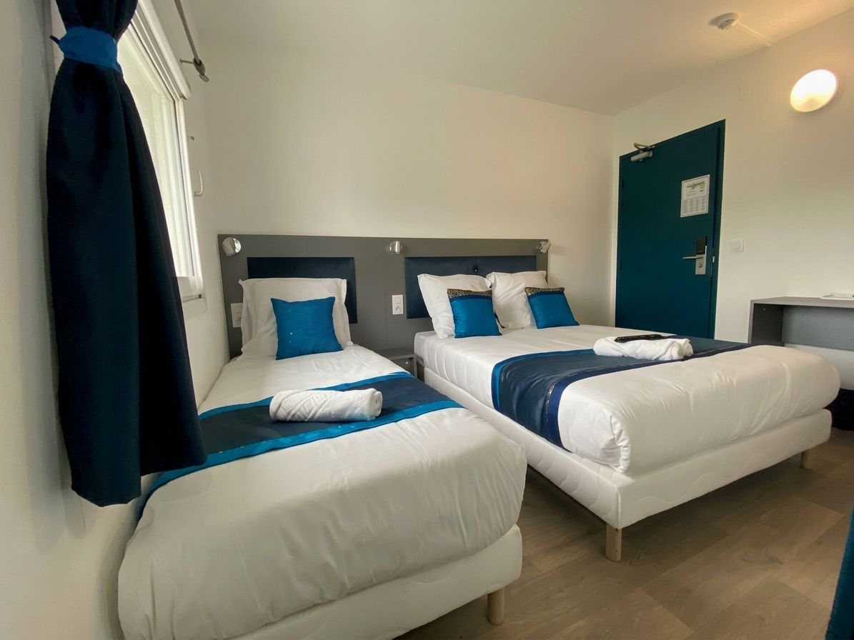 Ett hotellrum med två separata sängar, ett skrivbord och en dörr.
