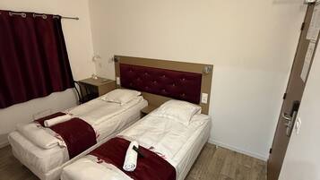 A hotel room with two single beds, a wooden floor, a red curtain, and a white wall.