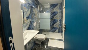 Une salle de bain avec un mur en marbre, un lavabo blanc, des toilettes et une baignoire.