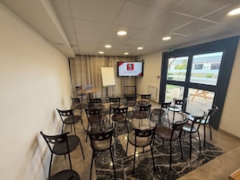 Un salón de conferencias con una pizarra, una computadora portátil sobre una mesa y una pantalla de televisión mostrando un logotipo.