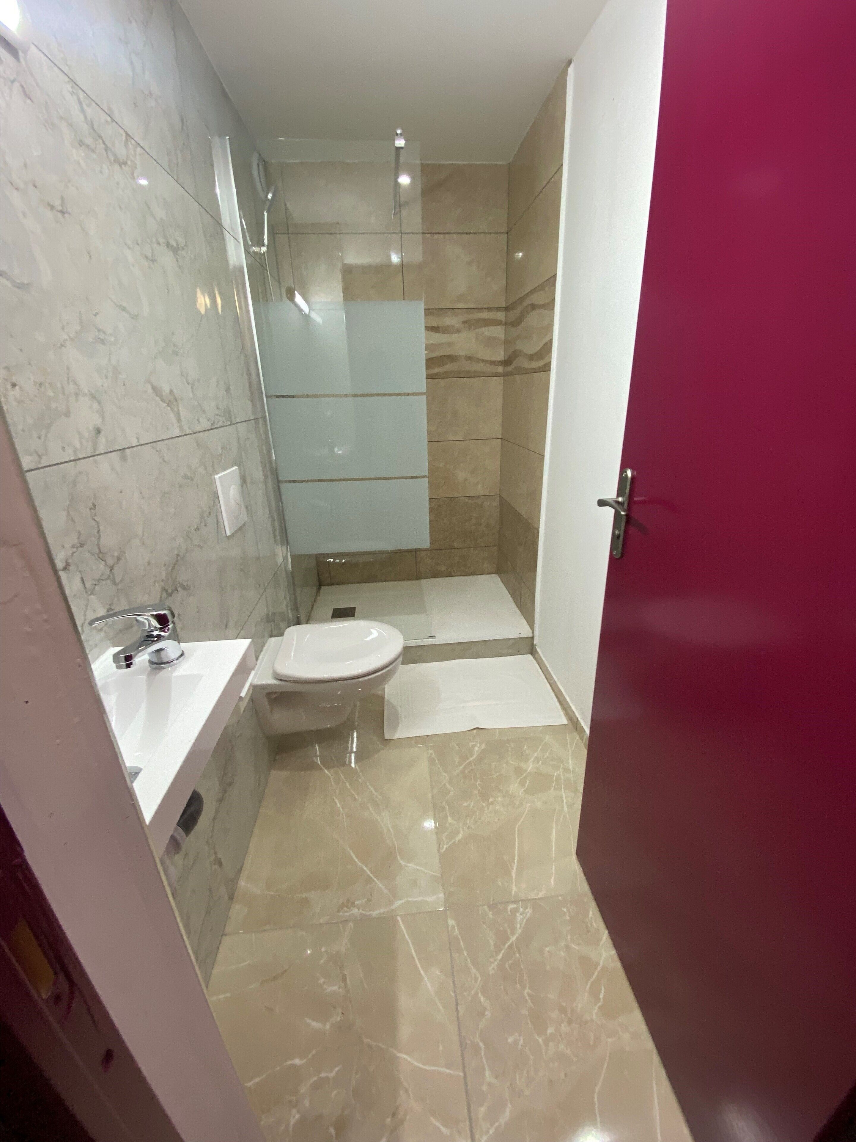 A modern bathroom with a marble floor, a white sink, a toilet, and a glass shower enclosure.