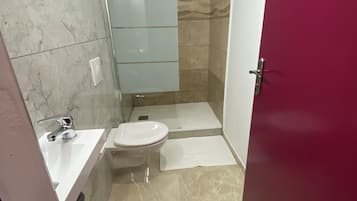 A modern bathroom with a marble floor, a white sink, a toilet, and a glass shower enclosure.