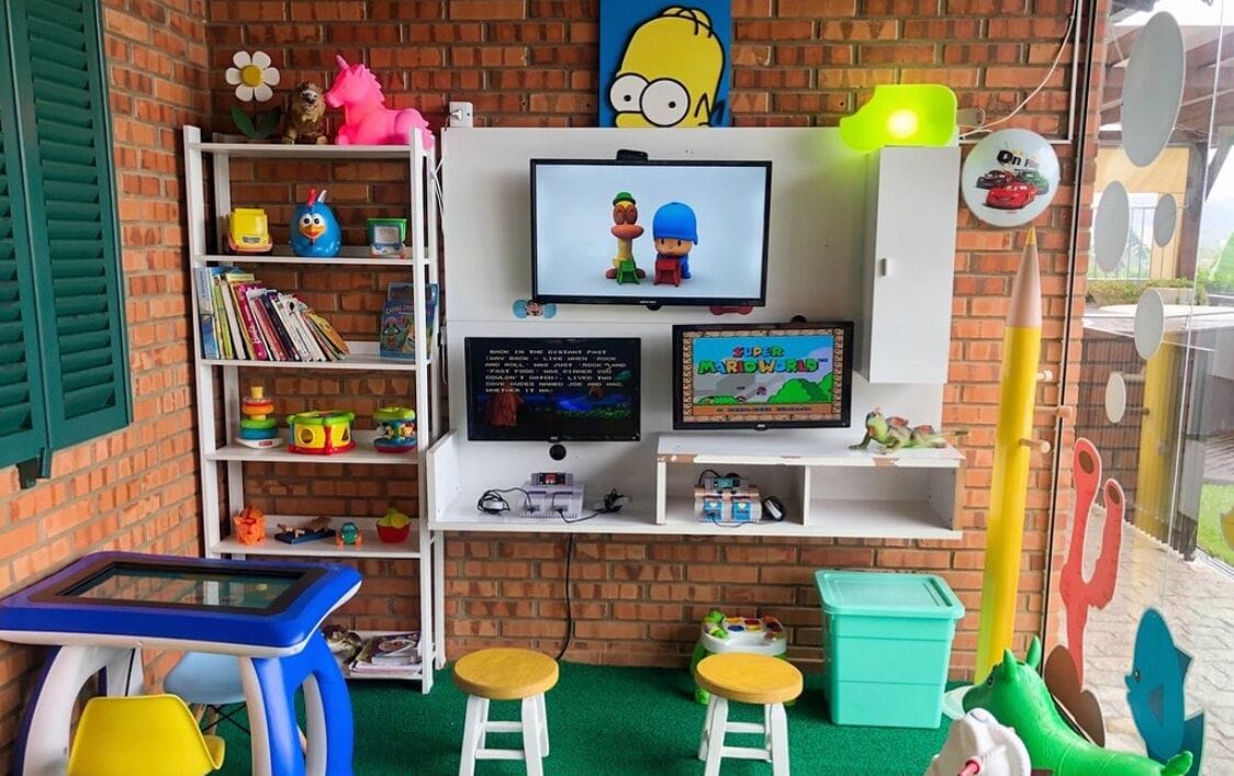 Ein Kinderspielbereich mit Fernseher, Regalen voller Spielzeug und einem Tisch mit Hocker.