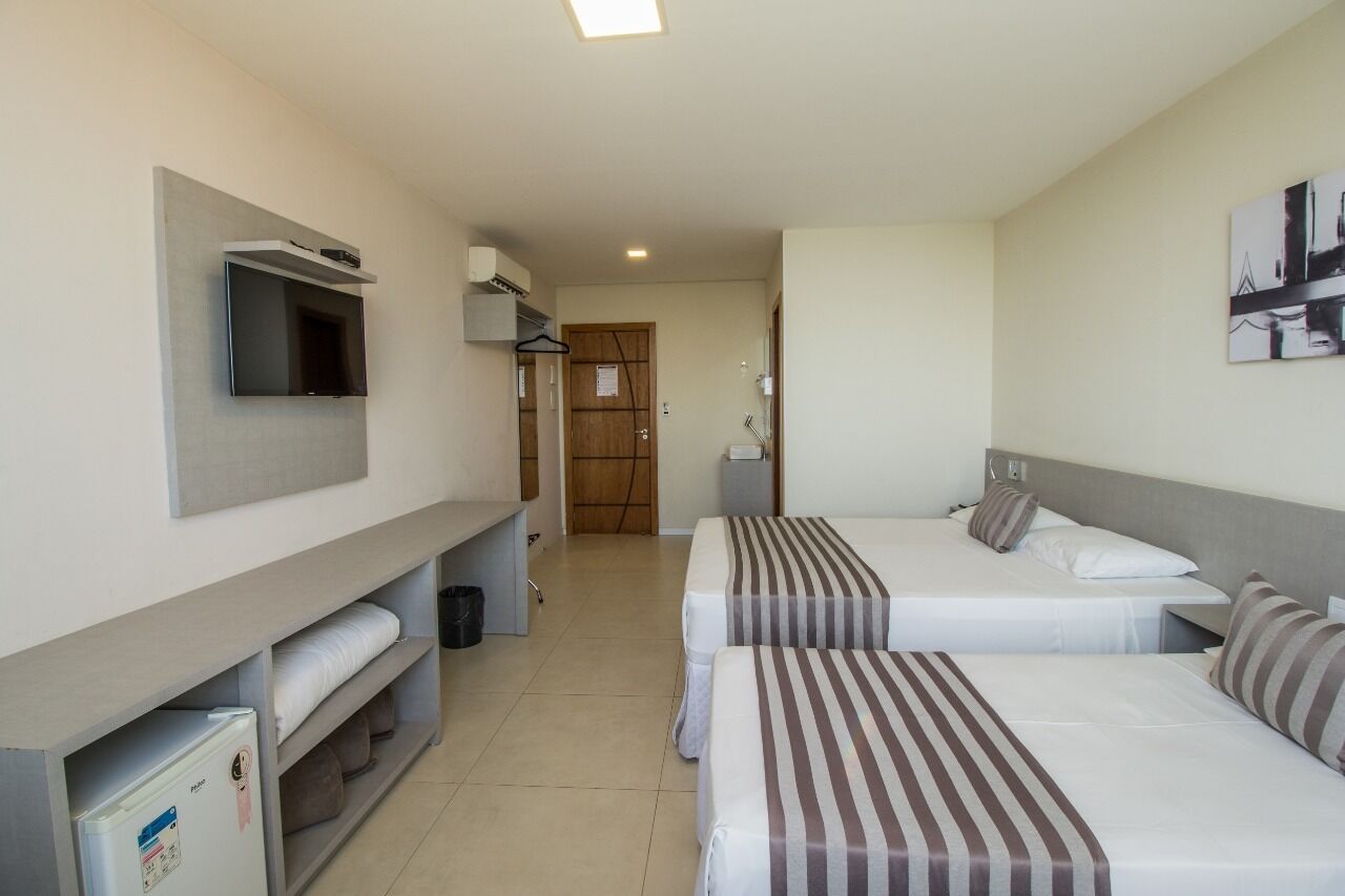 A hotel room with two beds, a TV mounted on the wall, a small desk, and a refrigerator.