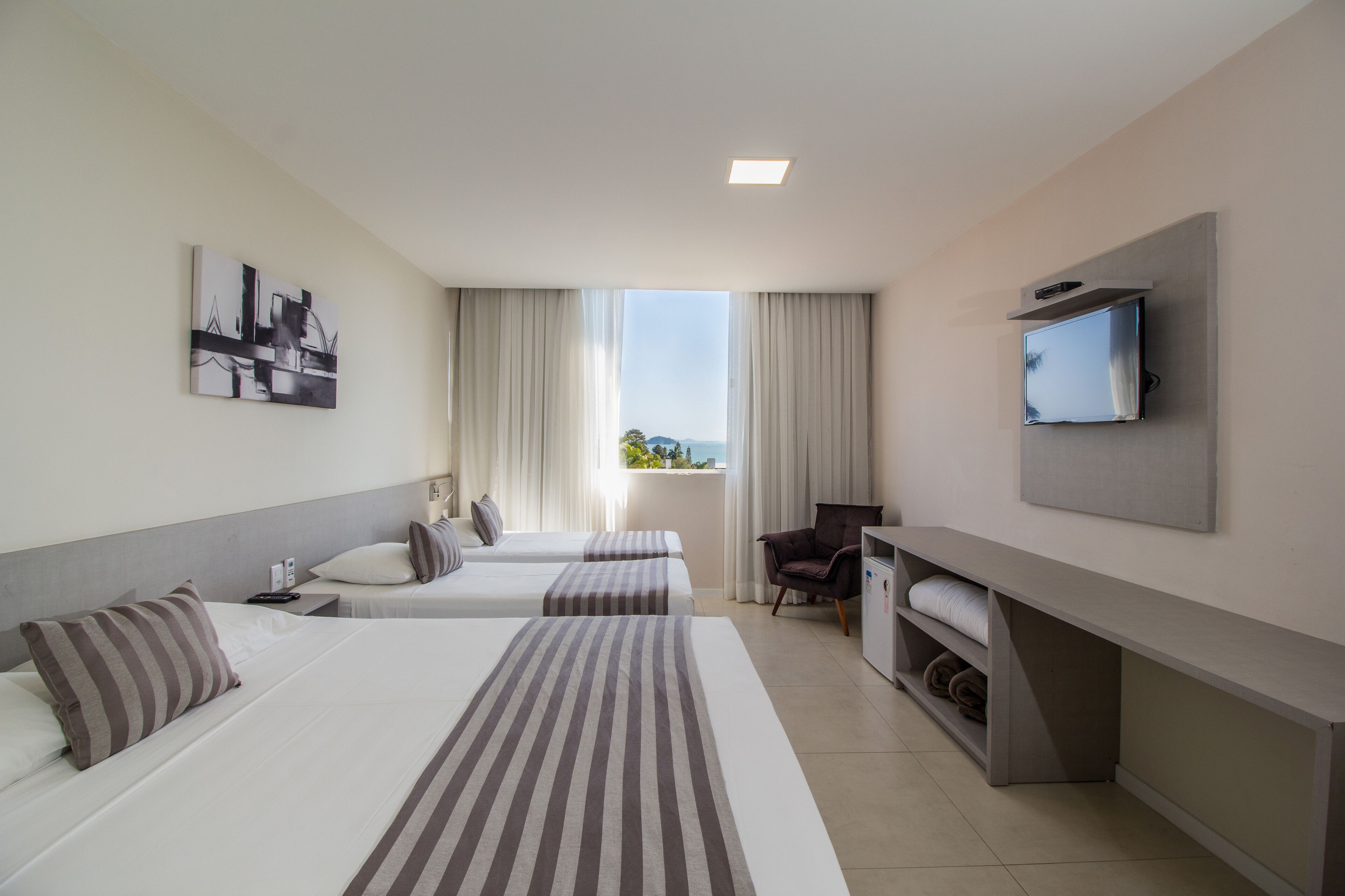 A hotel room with two beds, a TV, a desk, and a window with curtains.