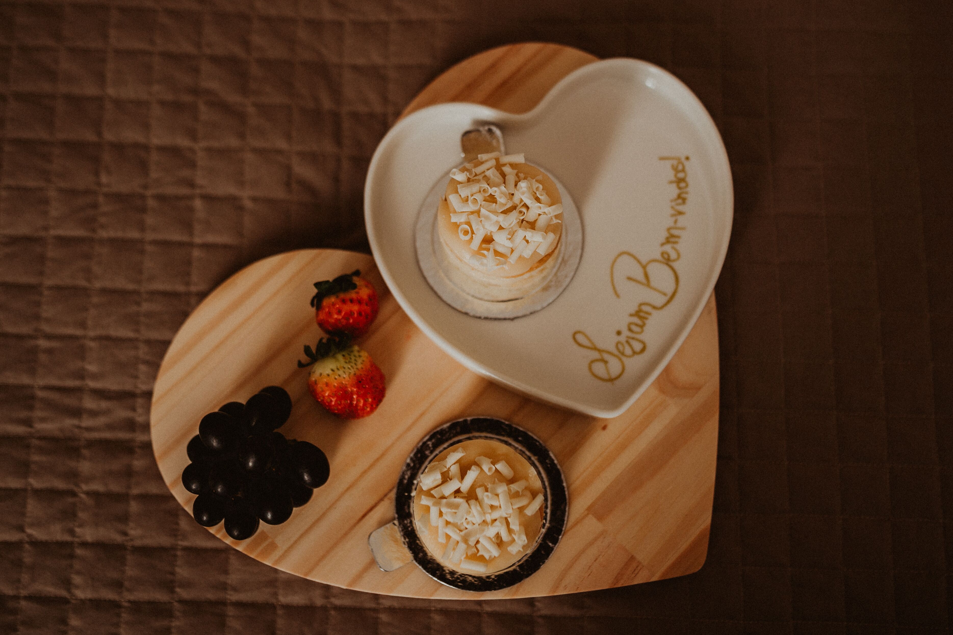Un plato con forma de corazón, un postre y fresas sobre una superficie de madera.