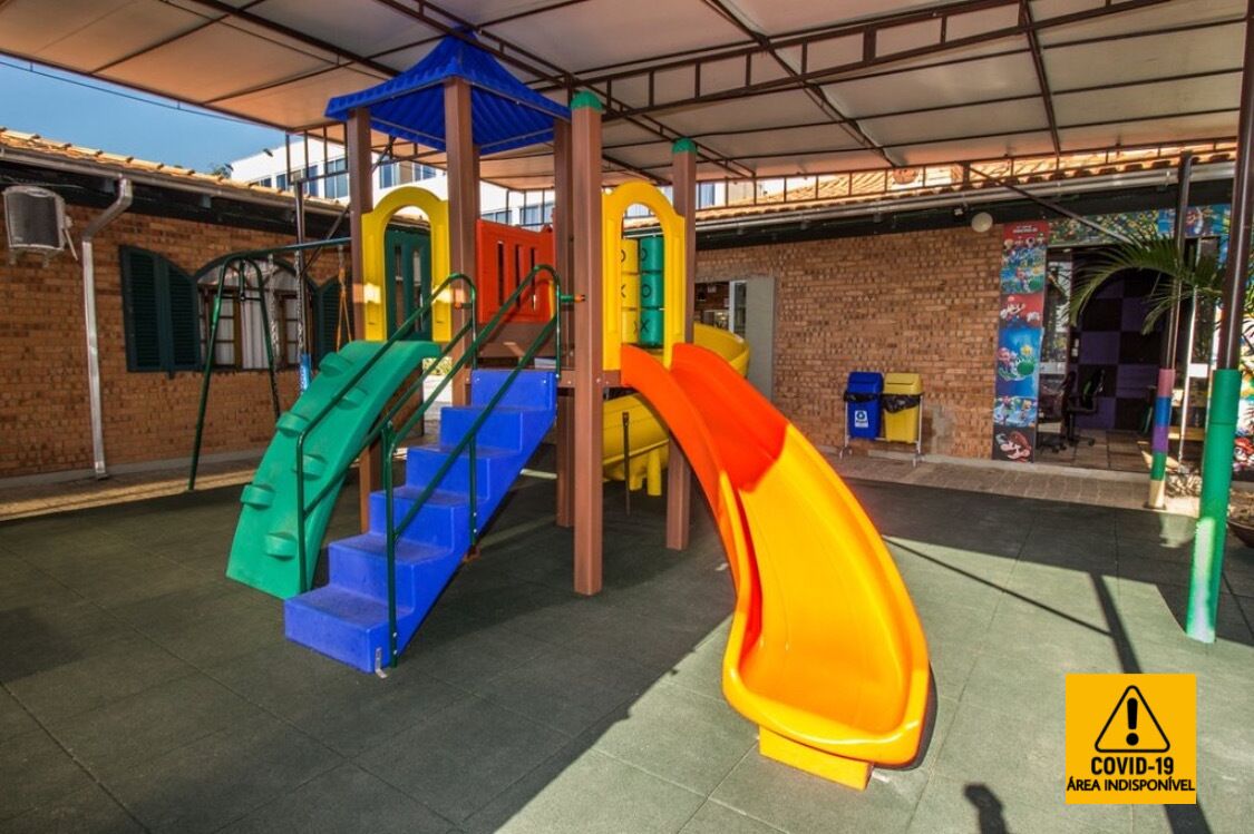 A playground with slides and climbing structures, surrounded by a brick building and covered by a roof.