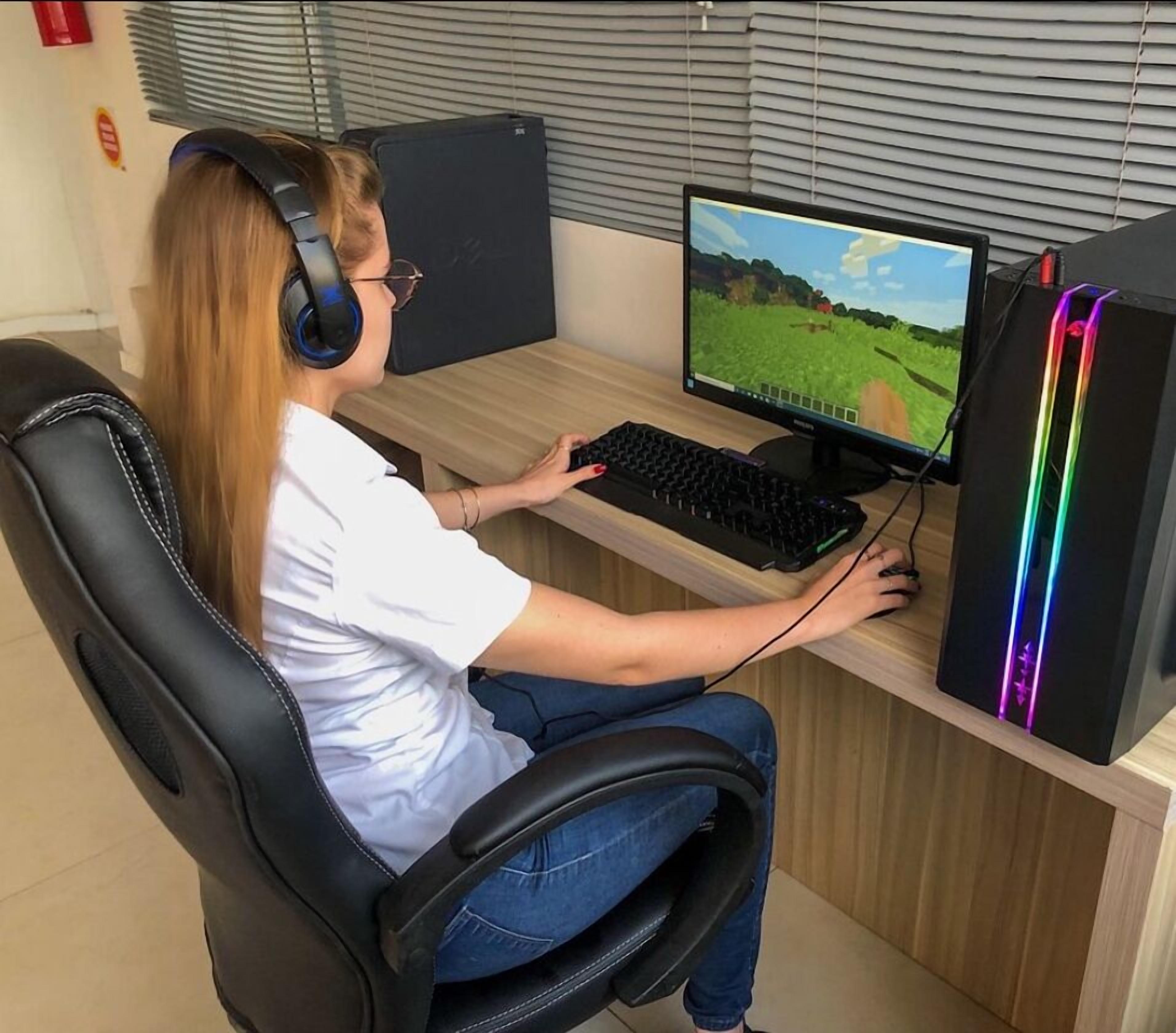 A person seated at a desk with a computer, headphones, and a keyboard.