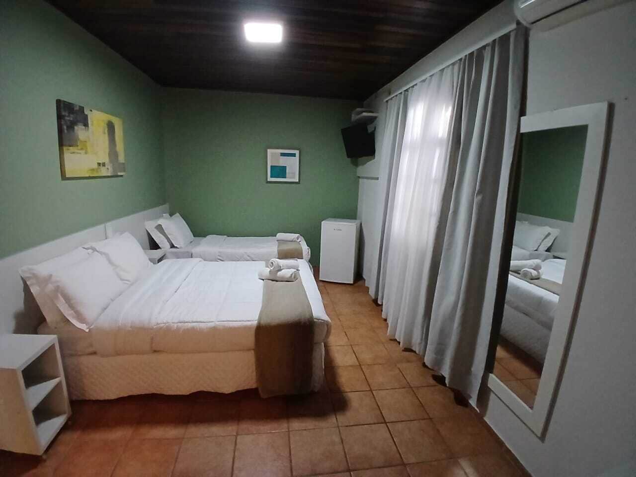 A room with two beds, a small table, a mirror, and a television on the wall.