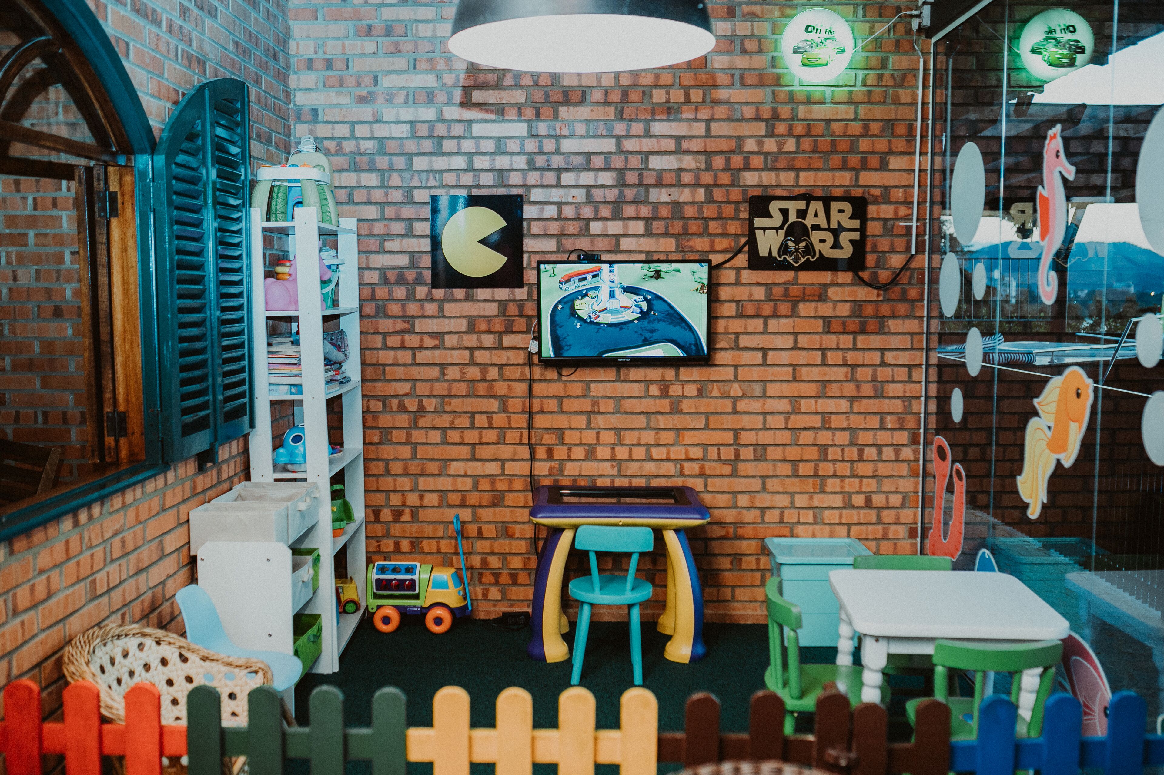 A children's playroom with a brick wall, Star Wars and Pac-Man decorations, a television, and a small table.