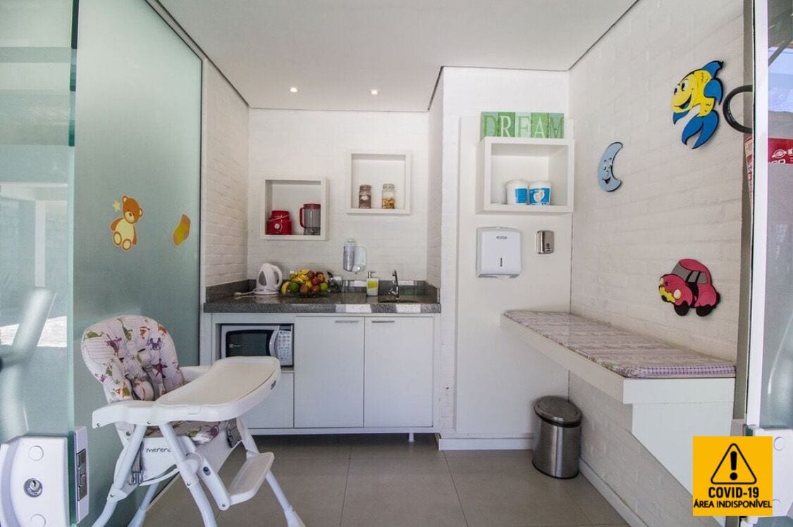 Cocina compacta con una trona, un lavamanos y una encimera con hervidor y frutero.