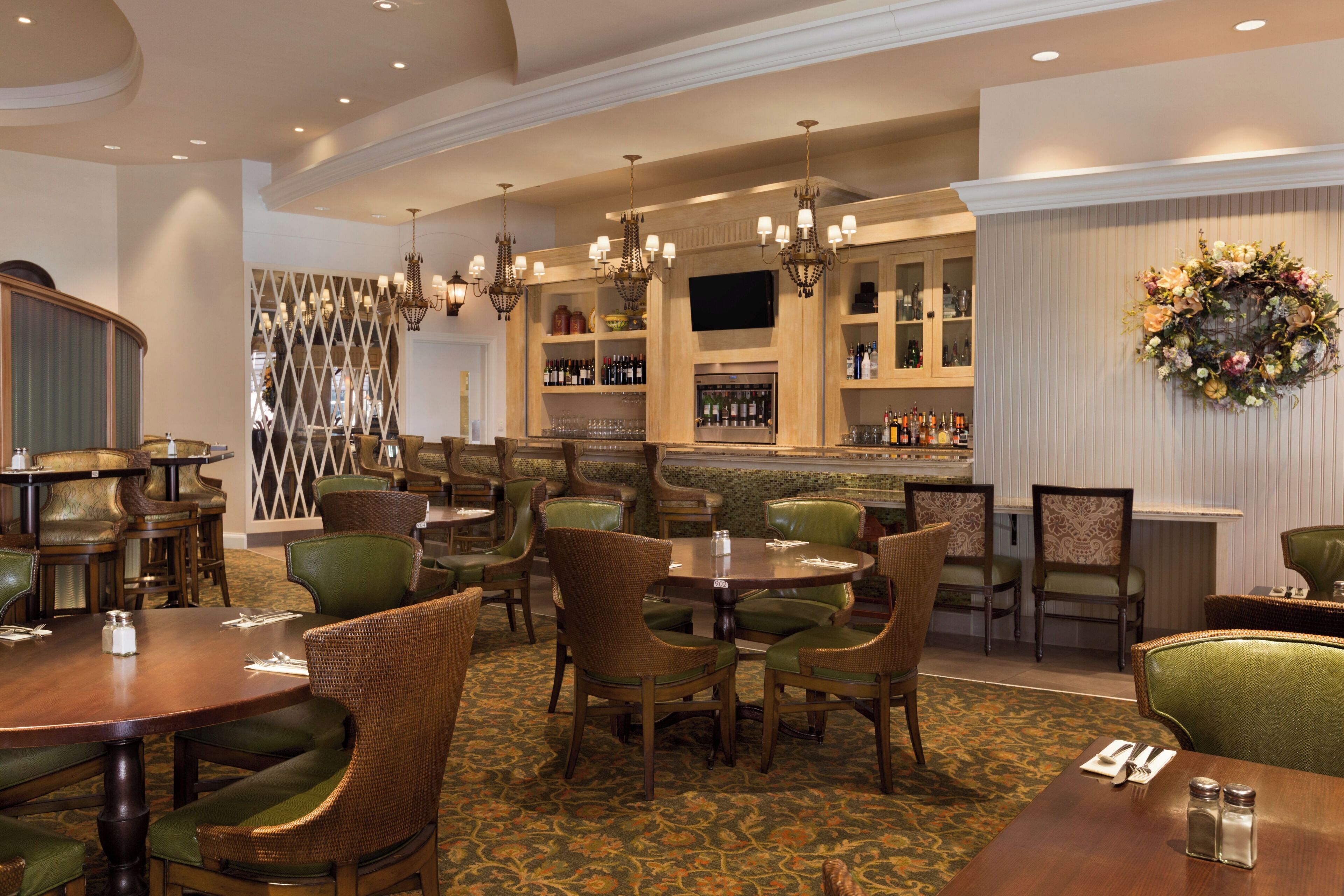 A restaurant with multiple dining tables and chairs, a bar area with a variety of bottles, and a decorative wall hanging.