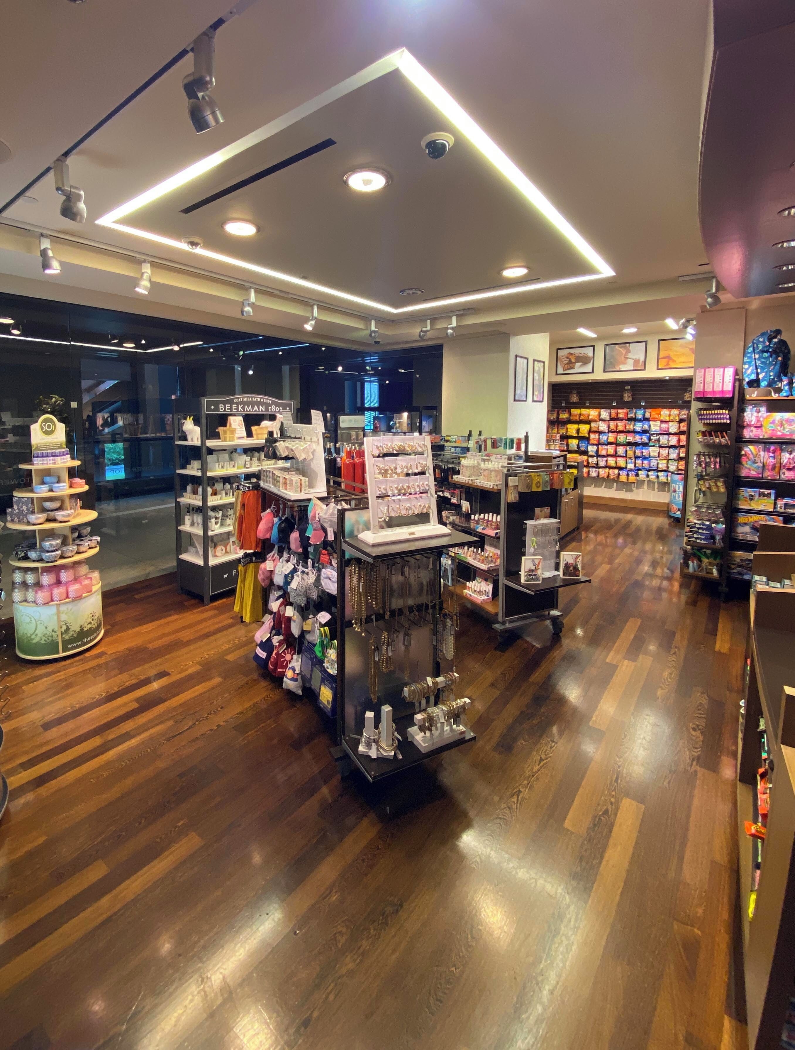 A modern retail store with wooden flooring, well-lit with ceiling lights, and various product displays including jewelry and bags.