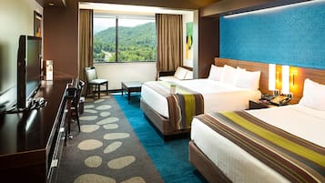 Habitación de hotel con dos camas, un escritorio, un televisor y vistas a un paisaje montañoso.