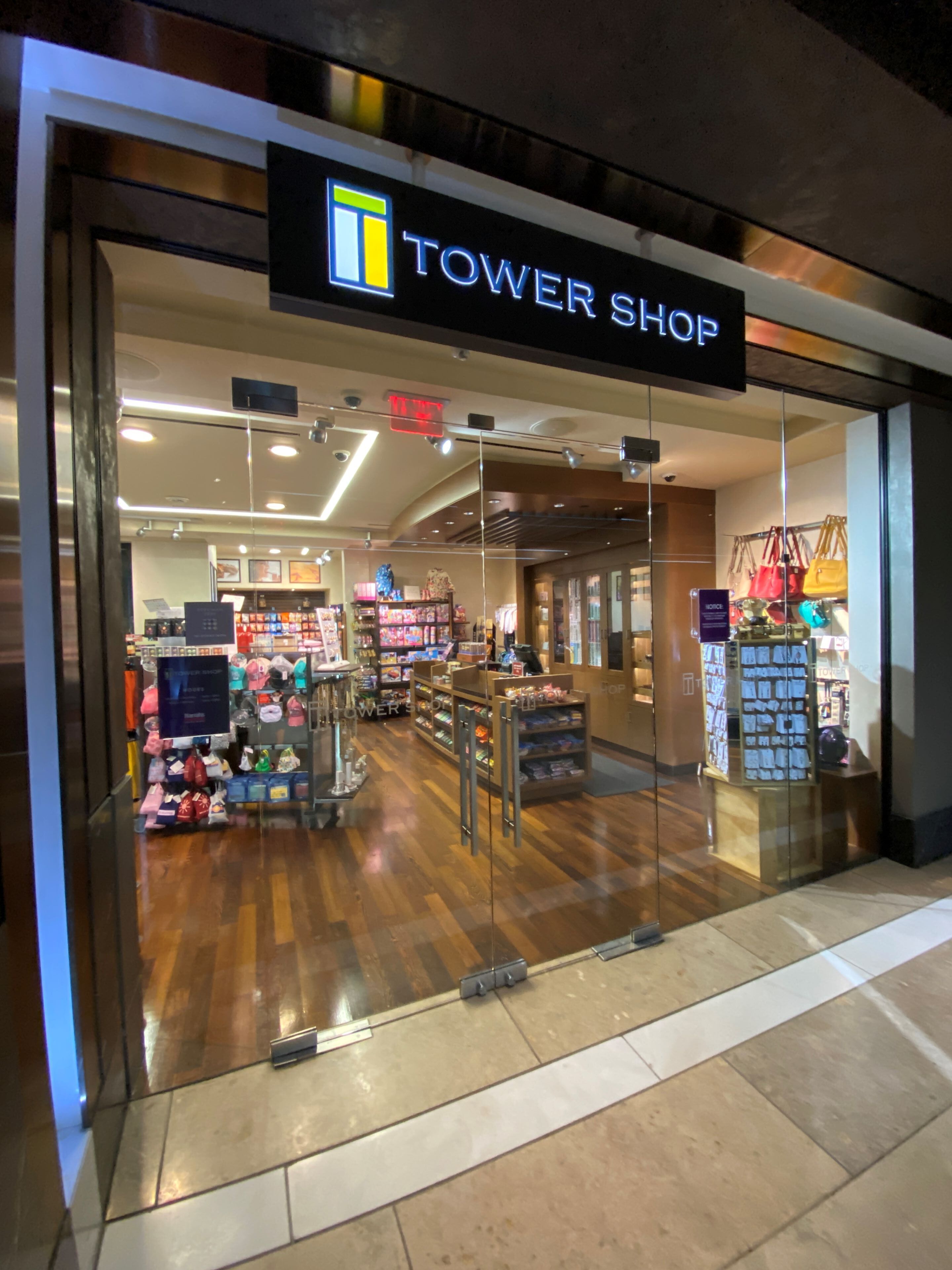 Uma loja chamada TOWER SHOP, com interior moderno, vitrines de vidro e diversos produtos nas prateleiras.