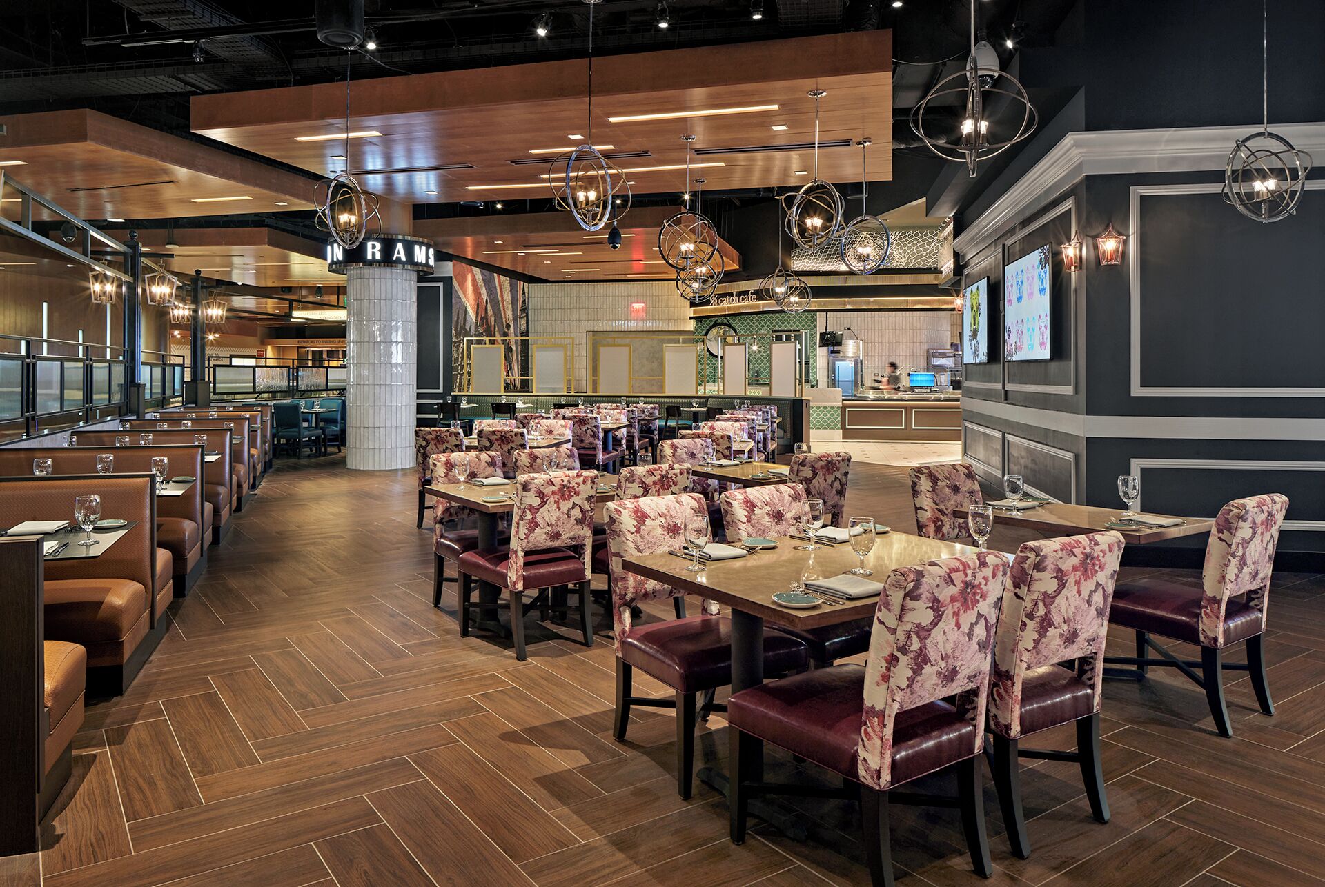 A restaurant with booths and tables, wooden flooring, and hanging pendant lights.