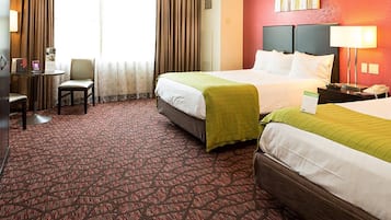 Quarto de hotel com duas camas, uma mesa, uma cadeira, um abajur e uma janela com cortinas.