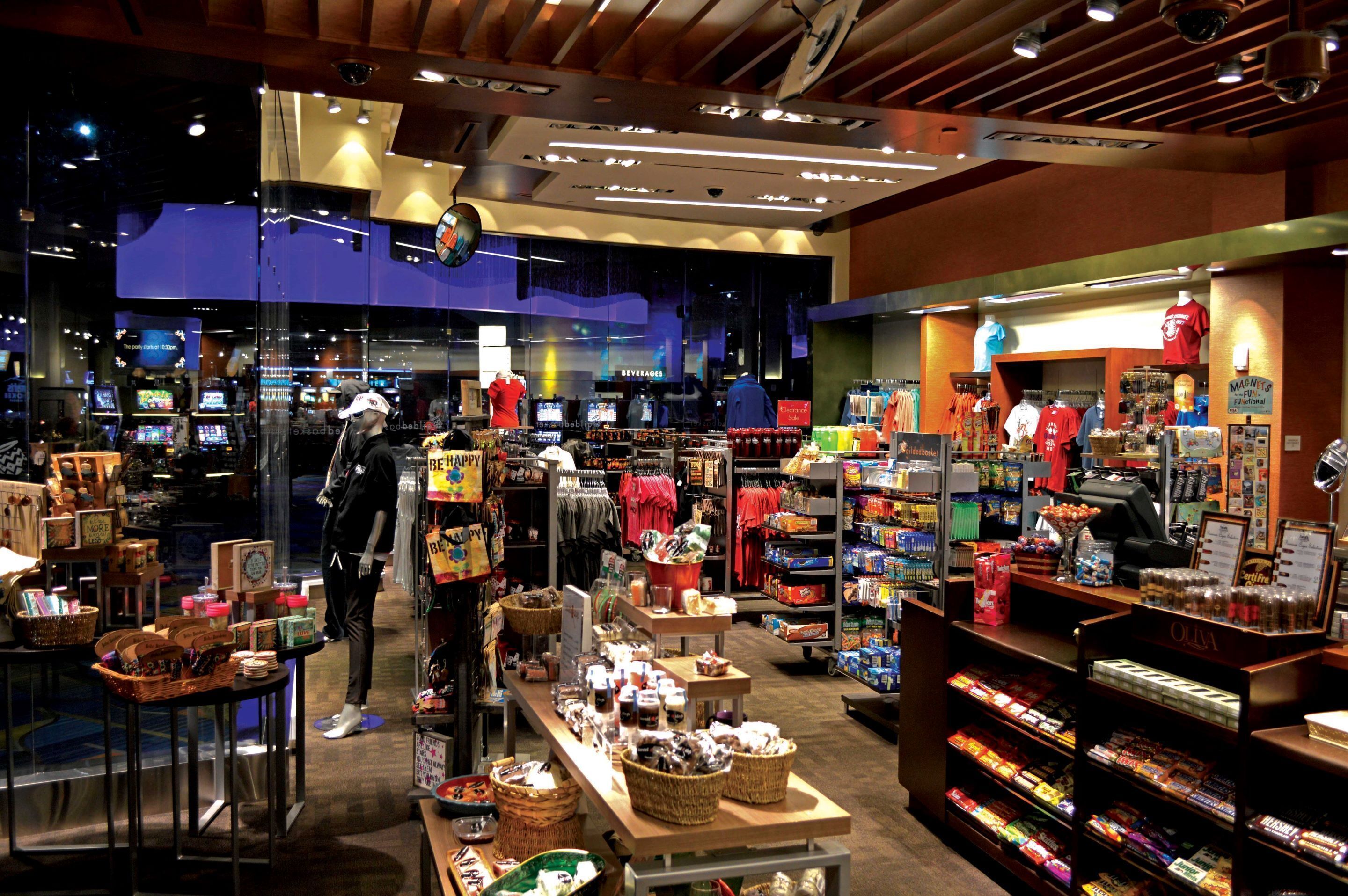 Un magasin bien éclairé où l’on trouve divers produits exposés sur des étagères et des tables, notamment des collations, des boissons et des vêtements.