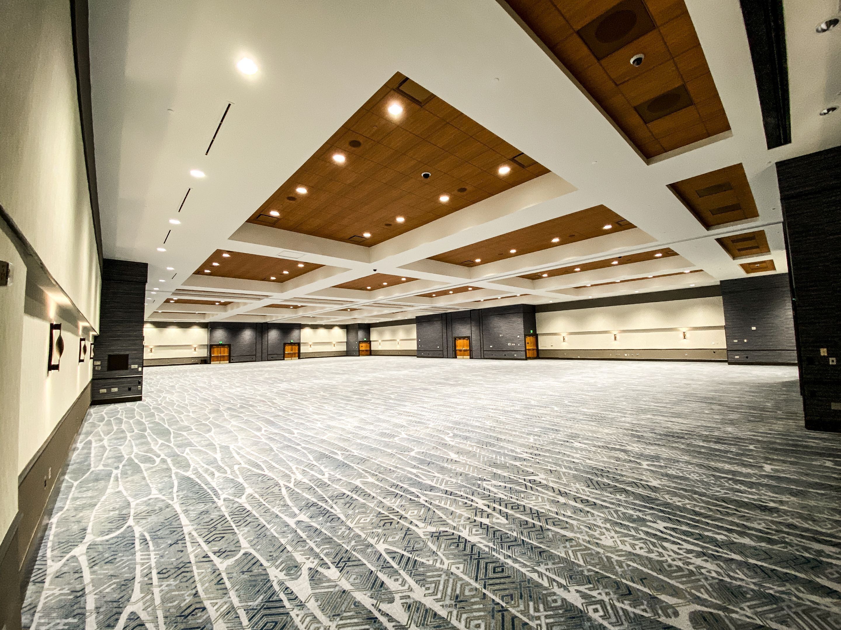 A large, empty conference room with a patterned carpet, wooden ceiling panels, and multiple doors along the walls.