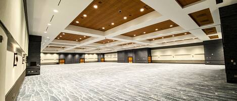 A large, empty conference room with a patterned carpet, wooden ceiling panels, and multiple doors along the walls.