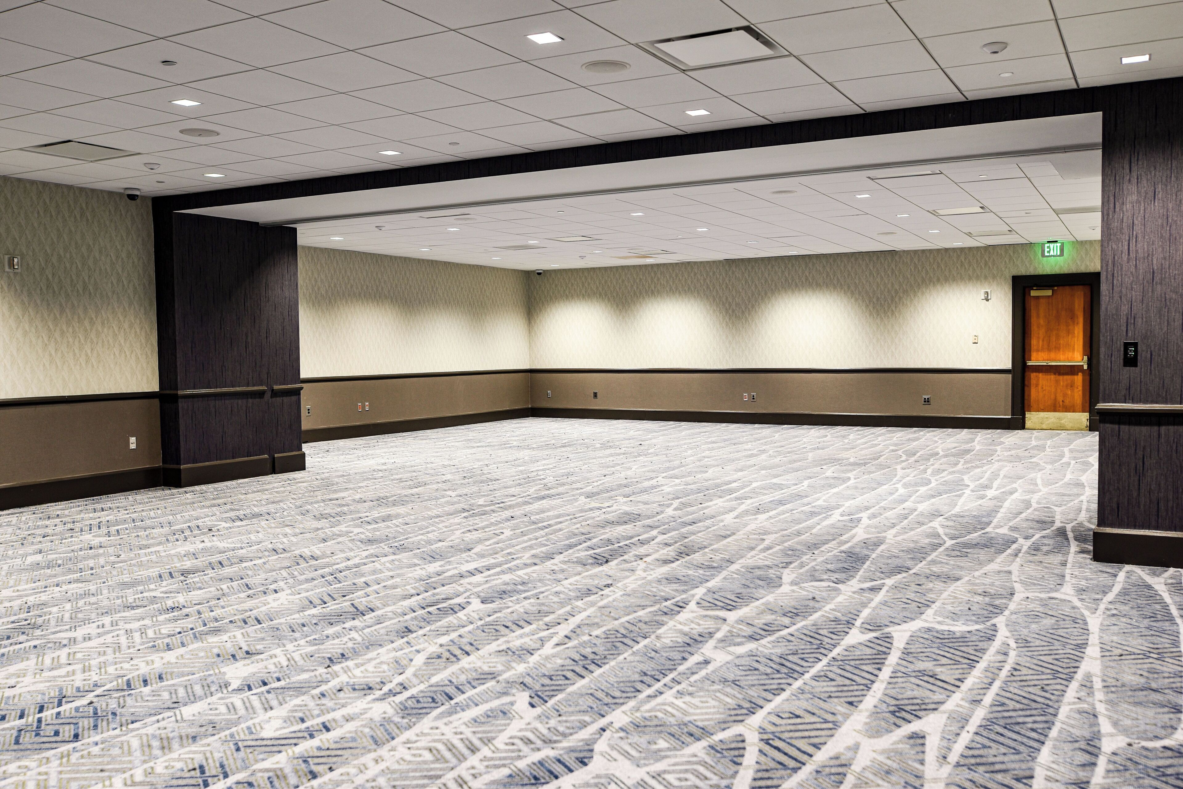 A large conference room with a patterned carpet, dark wood paneling on the walls, and a door with an exit sign.