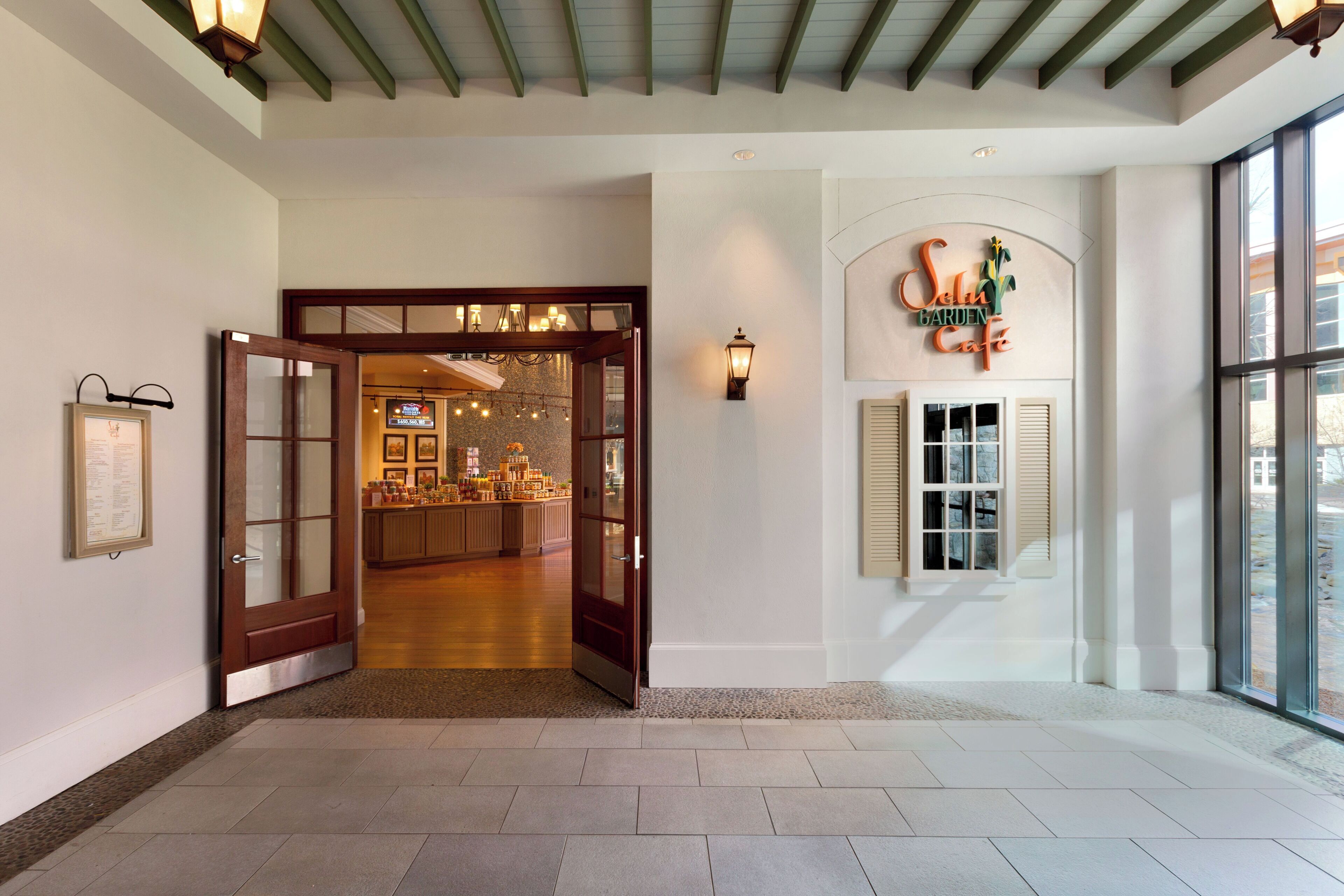 A hotel lobby with a wooden door leading to a bar area, a wall-mounted sign reading 'Solu Garden Cafe', and a large window with blinds.