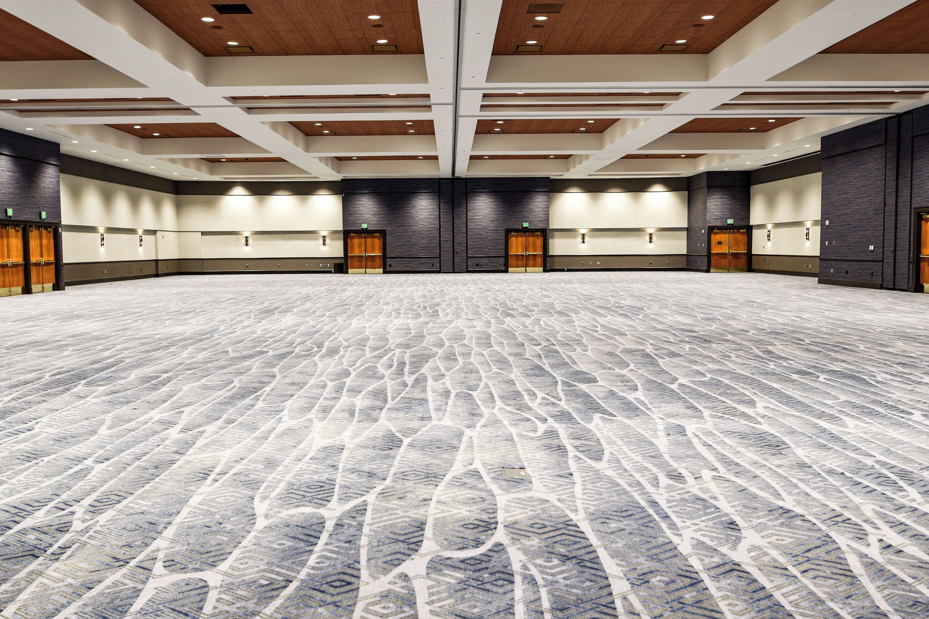 Une grande salle de conférence dotée d’un tapis  à motifs, de plusieurs portes et d’un plafond haut avec des luminaires encastrés.