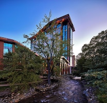 A modern building with a river in front, surrounded by trees.