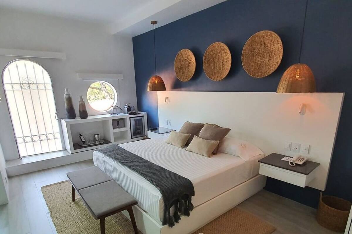 Ein modernes Schlafzimmer mit einem großen Bett, Nachttischen, einer Bank und Blick ins Freie durch ein Fenster mit Gitterstäben.