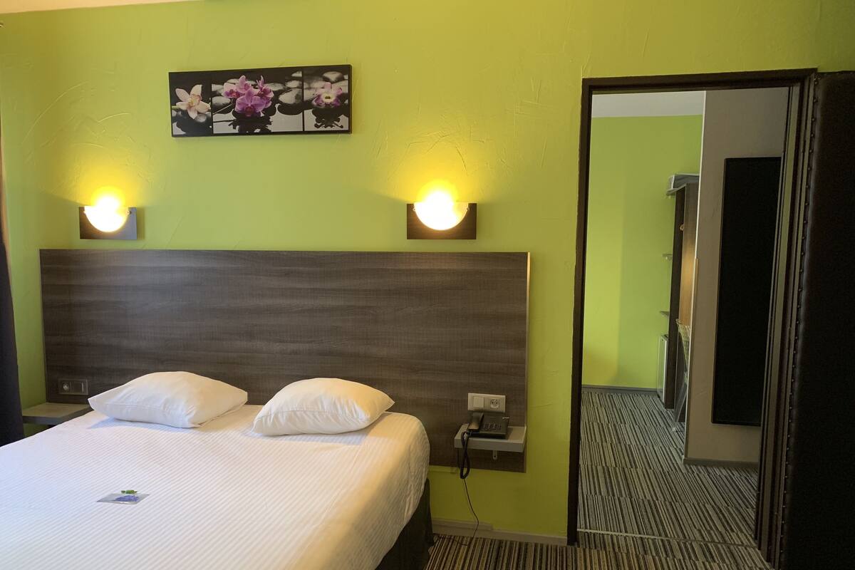 Quarto de hotel com uma cama grande, duas luminárias de cabeceira, uma mesa de apoio e um quadro pendurado na parede.
