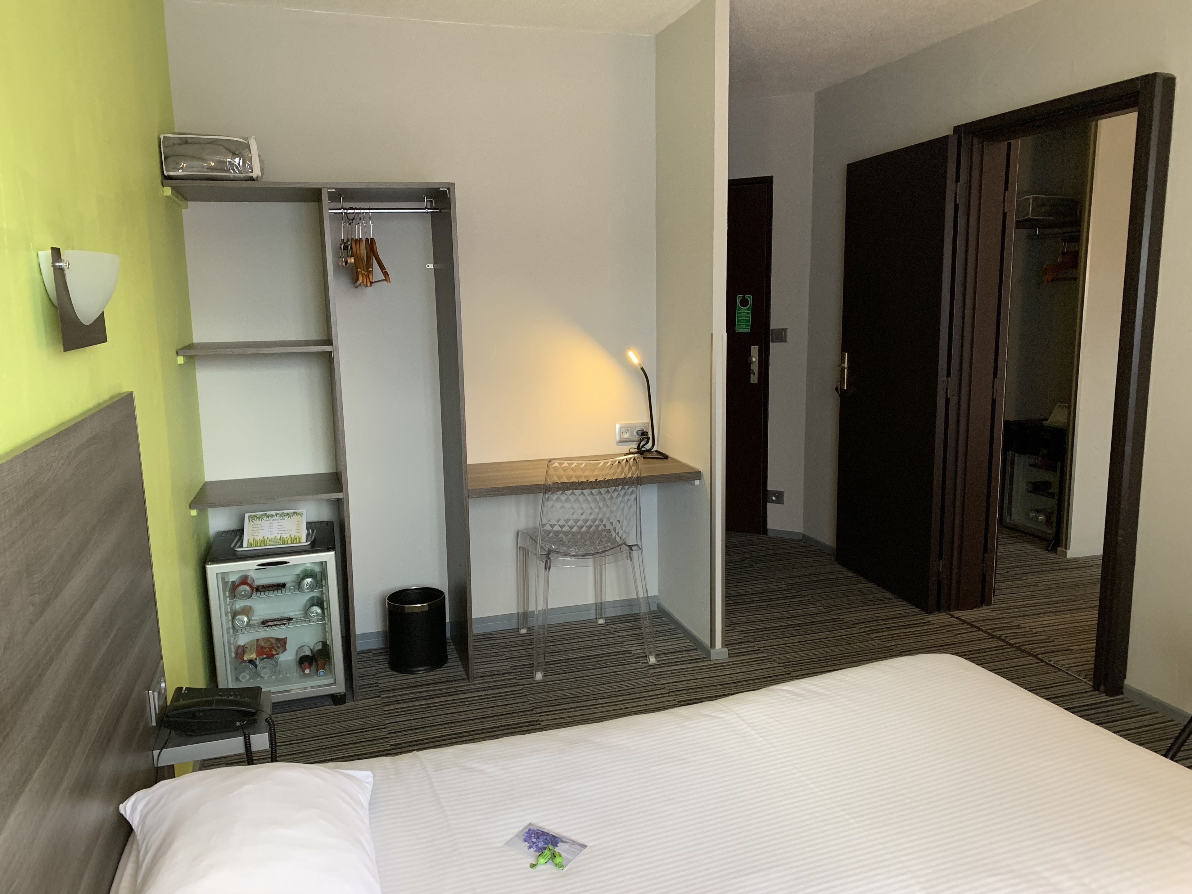 Une chambre d’hôtel comprenant un lit, un bureau avec une chaise, une armoire, une poubelle et un téléphone.