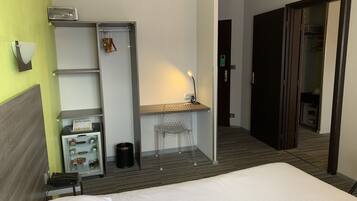 Une chambre d’hôtel comprenant un lit, un bureau avec une chaise, une armoire, une poubelle et un téléphone.