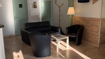Un espace d’accueil comprenant un canapé, des fauteuils, une table basse, un téléviseur et un porte-manteau en bois.