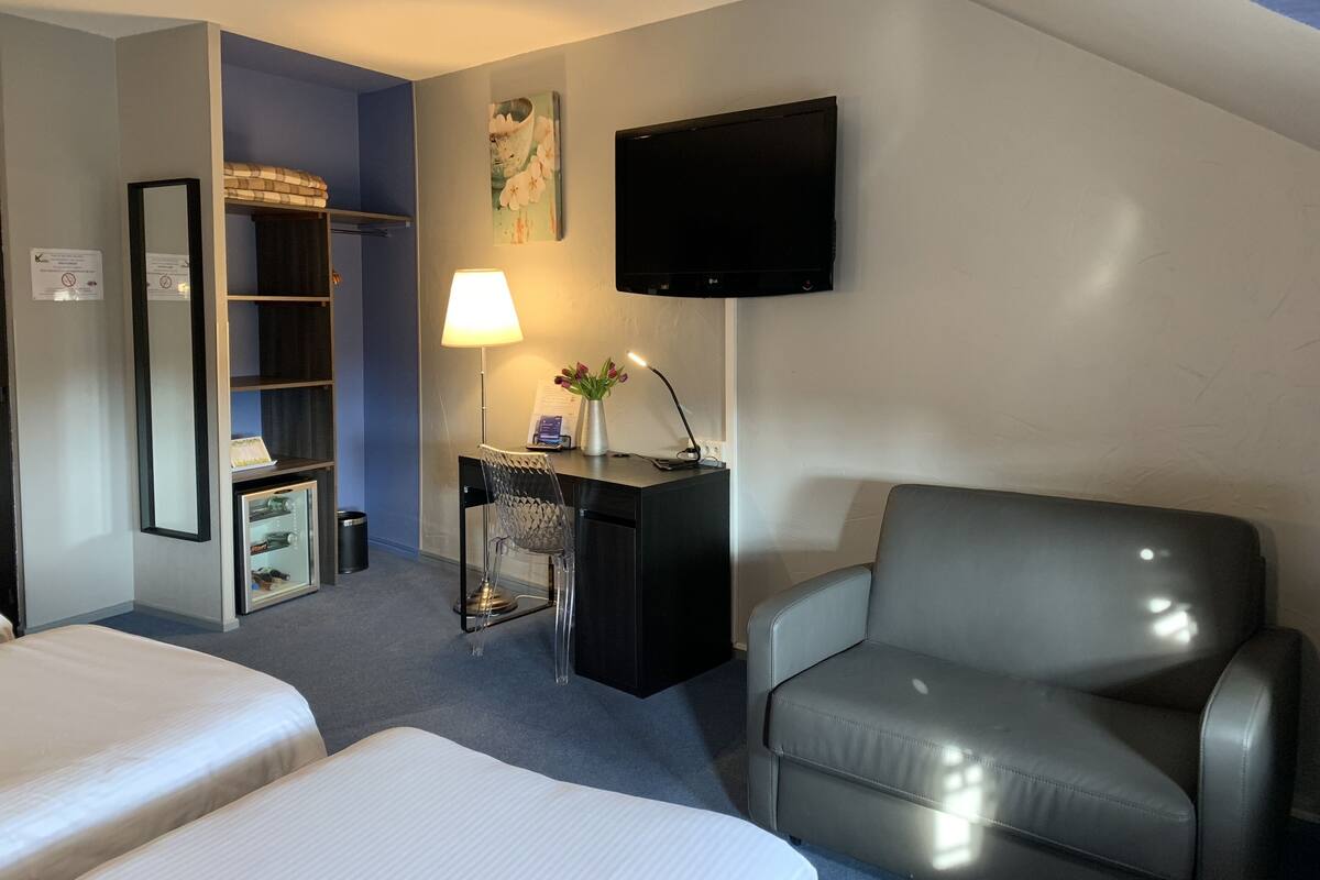 Quarto de hotel com duas camas, uma escrivaninha com luminária, televisão e uma cadeira.