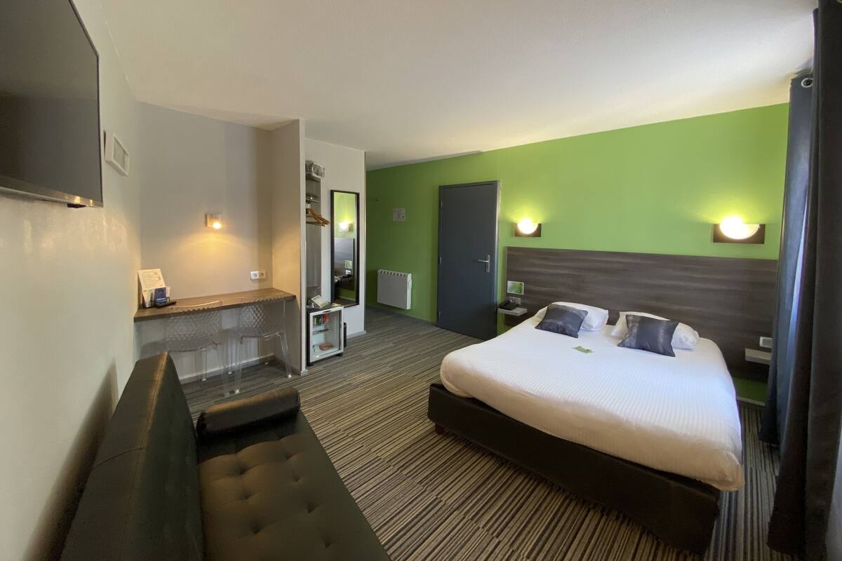 Quarto de hotel com cama, área de estar, espelho e escrivaninha.