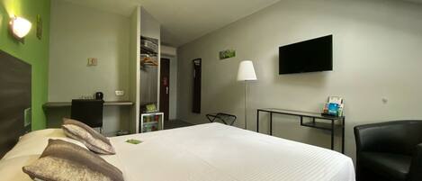 A hotel room with a large bed, a desk, a chair, a TV, and a wardrobe.
